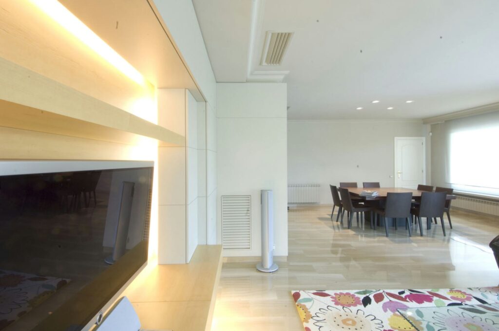Diseño de Interiores Moderno en Barcelona con Madera y Mármol Una sala de estar contemporánea en Barcelona con una unidad de entretenimiento de madera, iluminación LED, una alfombra vibrante, una elegante mesa de comedor y grandes ventanas que permiten la entrada de luz natural.