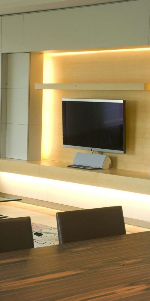 Espacio de vida contemporáneo en Barcelona que muestra un diseño de interiores minimalista, con una televisión montada en una pared de madera iluminada cálidamente, un elegante consola y una mesa de comedor moderna en primer plano.