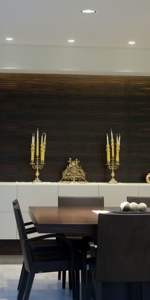 Un sofisticado área de comedor moderna que presenta una gran mesa de madera oscura con sillas negras, un armario contemporáneo con acabados de madera oscura y blanca, candelabros dorados decorativos y una encantadora pieza decorativa en forma de corazón.