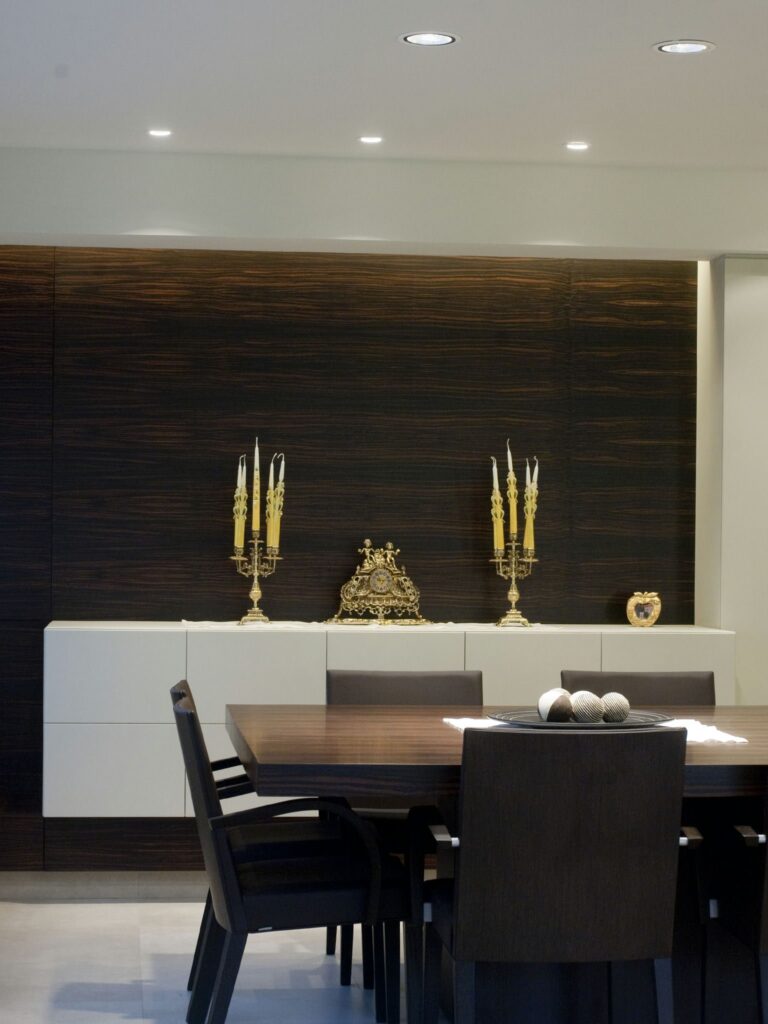 Área de Comedor Moderna y Elegante con Muebles de Madera Oscura y Acabados Dorados Un sofisticado área de comedor moderna que presenta una gran mesa de madera oscura con sillas negras, un armario contemporáneo con acabados de madera oscura y blanca, candelabros dorados decorativos y una encantadora pieza decorativa en forma de corazón.