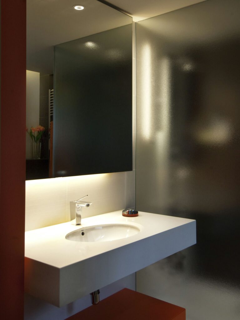 Diseño de baño moderno con elegante encimera blanca y lavabo redondo Baño contemporáneo que presenta una encimera blanca con un lavabo redondo y un grifo elegante, iluminación ambiental y un partition de vidrio esmerilado, adornado con flores frescas para un toque cálido.
