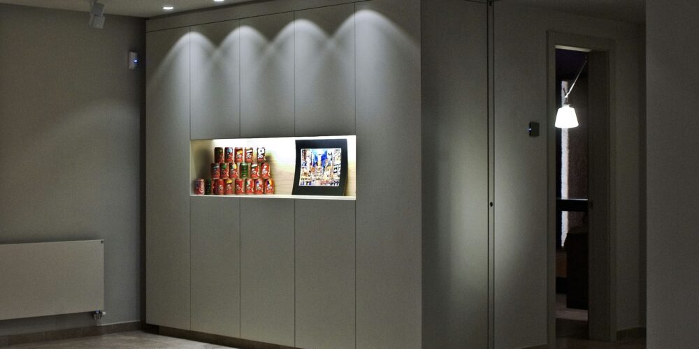 Un espacio interior moderno que presenta elementos de diseño minimalista, incluyendo un radiador montado en la pared, latas coloridas expuestas en la pared, obras de arte enmarcadas y un suelo de azulejos de color claro, creando una atmósfera cálida y acogedora.