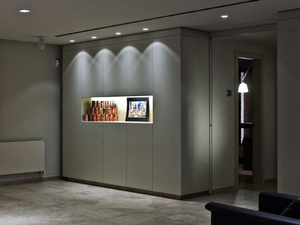 Diseño de Interiores Moderno Minimalista con Área de Exhibición y Radiador Montado en la Pared Un espacio interior moderno que presenta elementos de diseño minimalista, incluyendo un radiador montado en la pared, latas coloridas expuestas en la pared, obras de arte enmarcadas y un suelo de azulejos de color claro, creando una atmósfera cálida y acogedora.