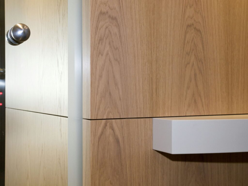 Diseño de Puerta Contemporánea con Texturas Mixtas Vista en primer plano de una puerta moderna que muestra un elegante pomo metálico, una superficie de color claro y un panel de madera con un patrón de vetas natural, destacando características de diseño contemporáneo.