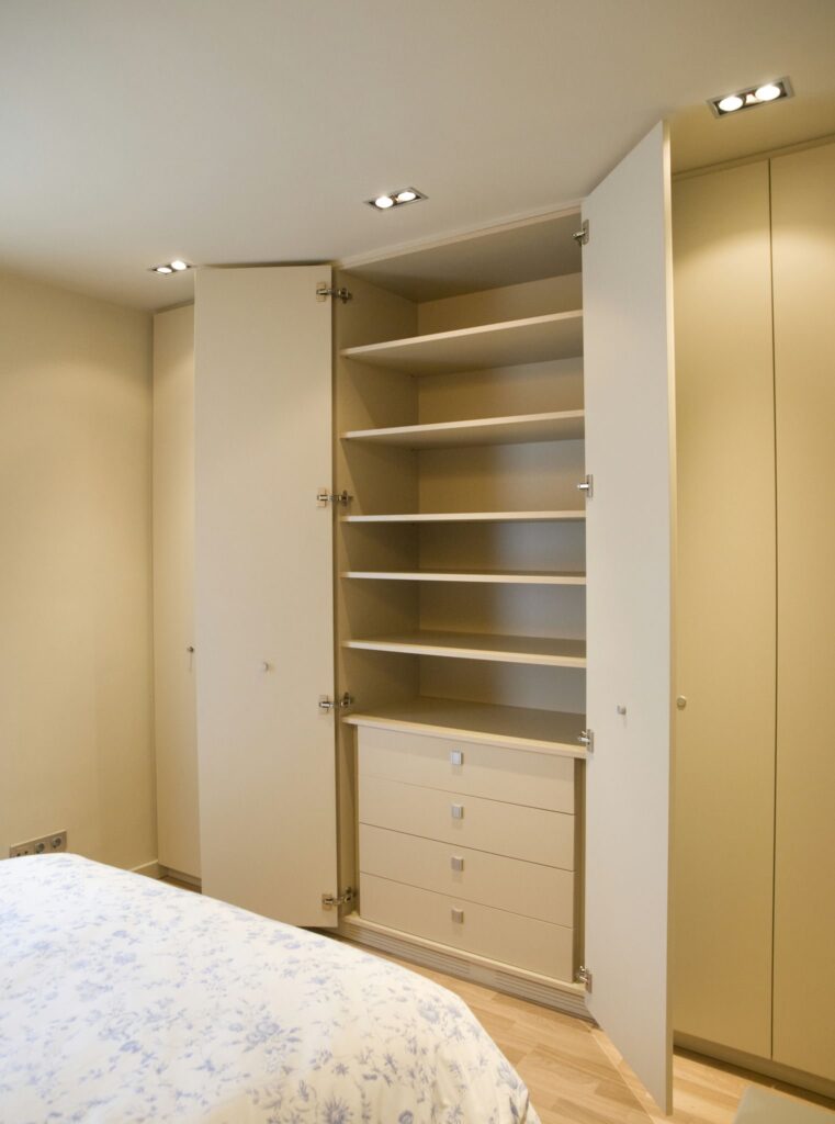 Diseño de Interiores Moderno en Barcelona: Armario Minimalista de Alta Gama Proyecto de diseño de interiores en Barcelona con un armario moderno que presenta estantes abiertos y cerrados. Combina funcionalidad y estética minimalista, utilizando colores claros y materiales de calidad como madera. La iluminación natural resalta la carpintería personalizada y los elementos de diseño contemporáneo.