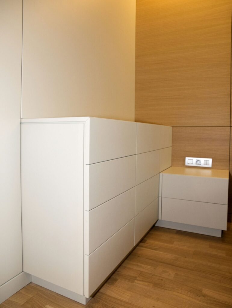 Diseño de gabinete minimalista contemporáneo en interior moderno Un elegante gabinete blanco con múltiples cajones y una pequeña unidad lateral en un espacio interior moderno que presenta una pared de madera y un cálido suelo de madera.