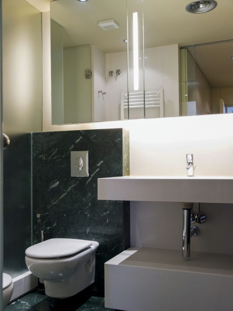 Baño moderno de alta gama en Barcelona con diseño arquitectónico elegante Diseño interior de baño contemporáneo en Barcelona, con paredes de mármol oscuro y elementos de lujo como un lavabo minimalista y un inodoro elegante, iluminado por luz natural.