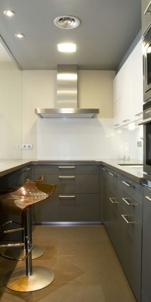 Un interior de cocina moderna que presenta muebles de gabinete gris oscuro, electrodomésticos de acero inoxidable y una encimera blanca elegante. El diseño incluye un backsplash minimalista, iluminación suave en el techo y grandes azulejos en el suelo, creando una atmósfera acogedora perfecta para comidas informales.