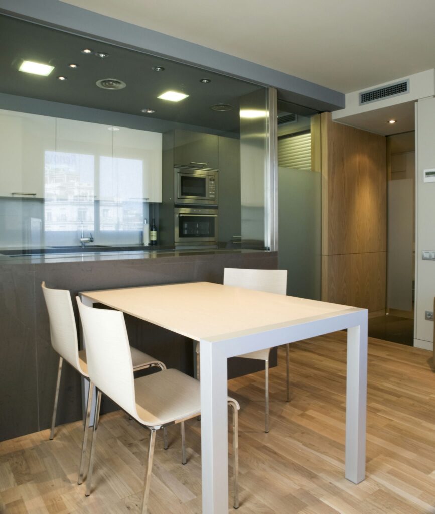 Piso en Av. Diagonal: Una cocina y comedor modernos y elegantes con un diseño minimalista, un suelo de madera clara, una mesa rectangular con cuatro sillas blancas y una cabinetry elegante.