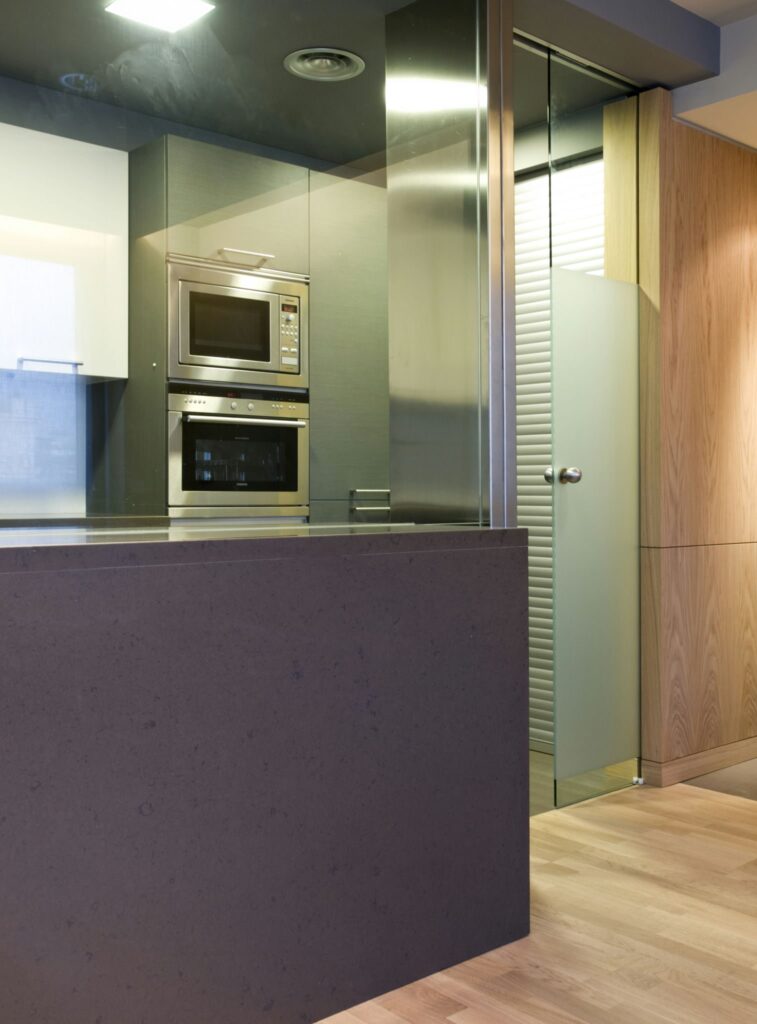 Cocina Moderna con Elementos de Diseño Elegantes y Estética Abierta Cocina contemporánea con encimera sólida oscura, electrodomésticos de acero inoxidable, mobiliario minimalista y suelos de madera aireados.