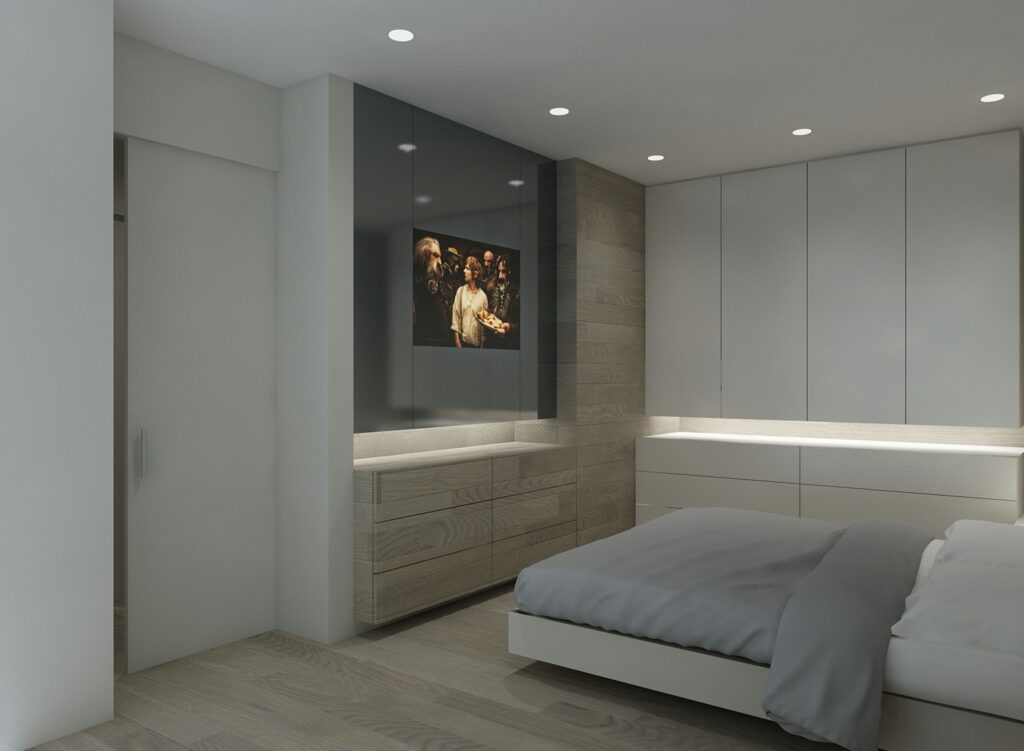 Diseño de interiores moderno en Barcelona: dormitorio elegante y funcional Dormitorio moderno en Barcelona con cama minimalista, ropa de cama gris suave, unidad de pared integrada y televisión montada. Espacio iluminado por luz natural y empotrada, resaltando materiales de alta calidad como madera y piedra, en un ambiente contemporáneo y sofisticado.