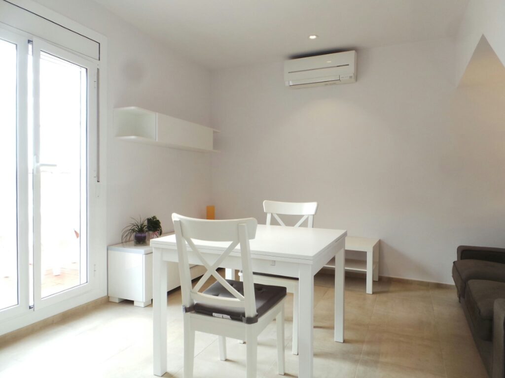 Interior de un elegante comedor moderno en Barcelona Espacio moderno de interior en Barcelona con un comedor elegante, mesa blanca y sillas oscuras, sofá gris, iluminación natural, y decoraciones minimalistas.