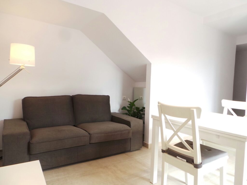 Diseño de interiores moderno en Barcelona: Sala de estar acogedora Interior moderno en Barcelona con un sofá gris, mesa de comedor blanca y silla estilizada, destacando la iluminación natural y materiales de calidad