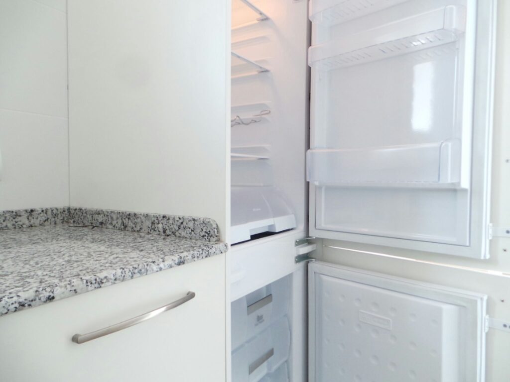 Cocina moderna con refrigerador blanco y encimera de mármol en Barcelona Cocina contemporánea con un elegante refrigerador blanco de puerta abierta, revelando su interior. Destacan la encimera de granito y el uso de materiales de alta calidad como mármol, en un espacio diseñado para resaltar la funcionalidad y la estética de interior en proyectos de alta gama en Barcelona.