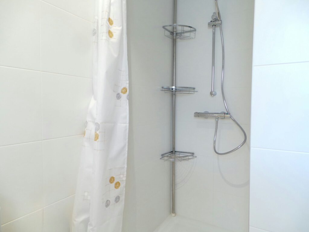 Diseño de interiores moderno en baño minimalista con ducha de lujo en Barcelona Espacio de ducha minimalista con azulejos blancos, grifo cromado, estanterías metálicas y cortina de ducha con patrón ligero, representando el diseño de interiores de alta gama en Barcelona.