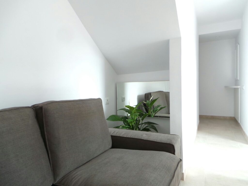 Diseño de interiores moderno en Barcelona: Sofá gris y detalles arquitectónicos sofisticados Interiores modernos en Barcelona con un sofá gris, planta interior y pasillo luminoso, destacando la funcionalidad, el uso de materiales de calidad y la iluminación natural.