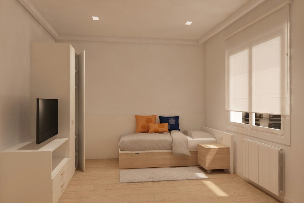 Dormitorio moderno y acogedor en Barcelona con paleta de colores claros Interior de dormitorio moderno en Barcelona con cama individual, cojines decorativos naranjas y azules, mesita de noche de madera y televisor en una unidad de medios blanca, iluminado por luz natural a través de una ventana con persianas claras.