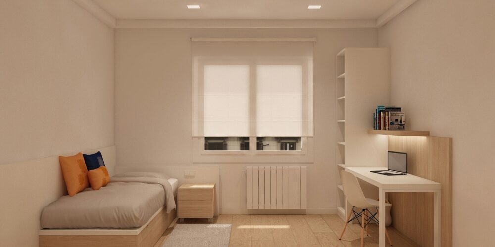 Dormitorio moderno en Barcelona con cama sencilla, cojines naranjas y azules, mesa de noche simple y escritorio con laptop. Espacio minimalista iluminado por luz natural, con suelo de madera y muebles elegantes que reflejan funcionalidad y estilo.