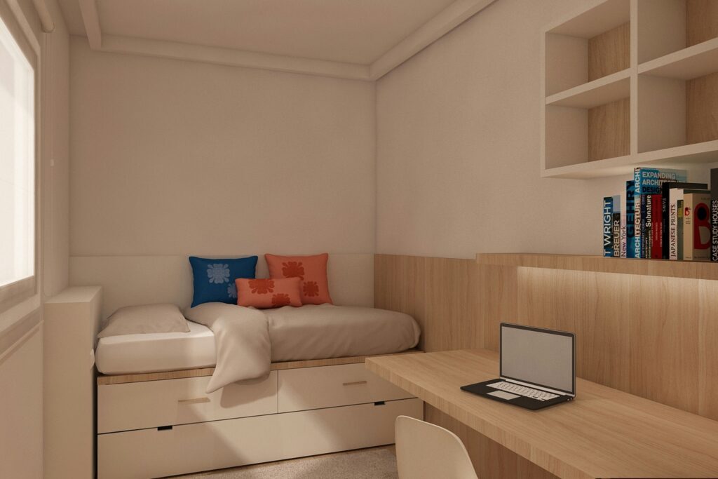 Diseño de interiores moderno en una acogedora habitación de Barcelona Proyecto de diseño de interiores moderno en Barcelona, mostrando una acogedora habitación con una cama estilizada, cojines decorativos coloridos, un escritorio elegante con laptop, y detalles en madera que resaltan la luz natural.