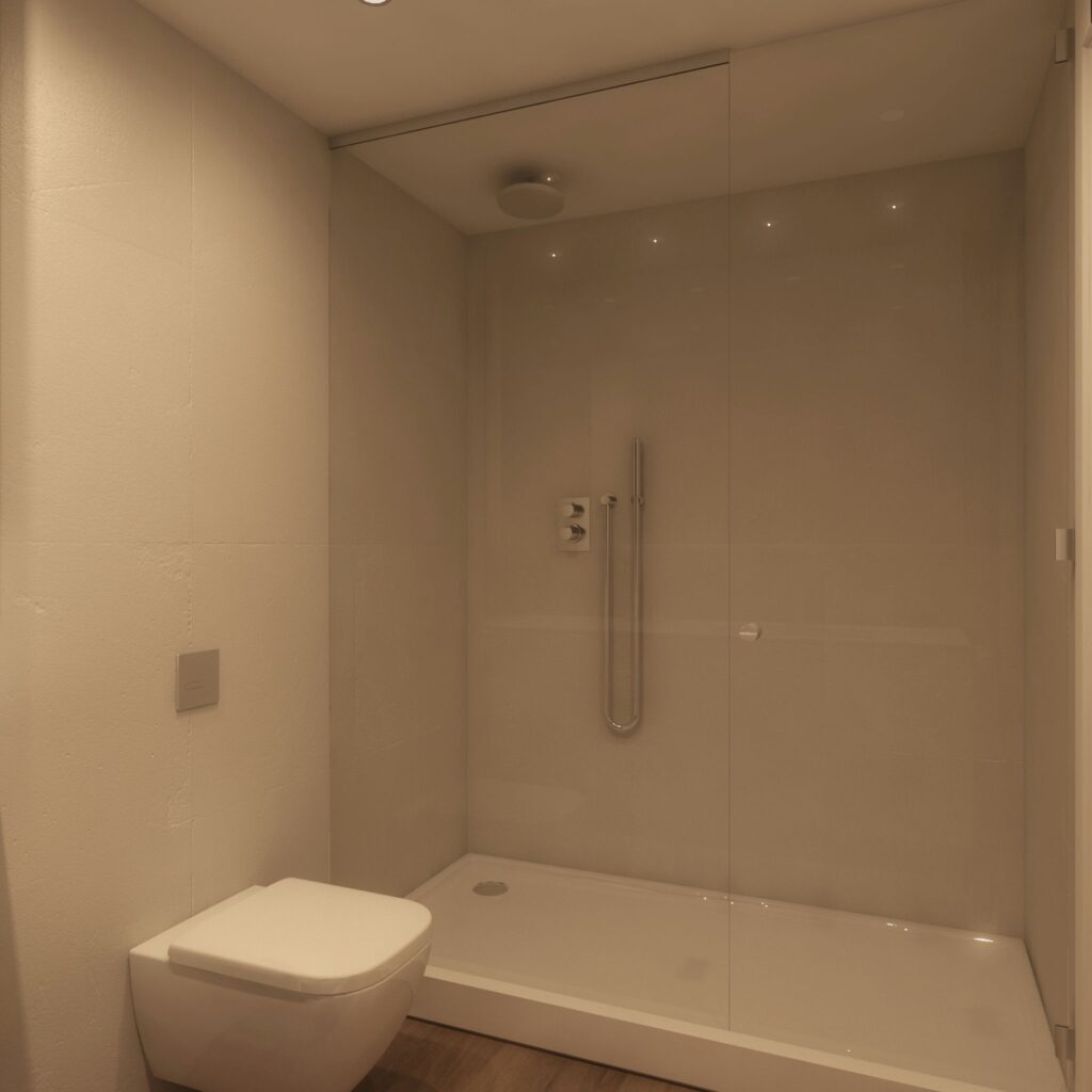 Baño Moderno con Ducha de Vidrio en Proyecto de Diseño de Interiores en Barcelona Espacio de baño moderno en Barcelona, destacando una amplia ducha de vidrio, inodoro contemporáneo y suelo claro, con detalles minimalistas y alta funcionalidad.