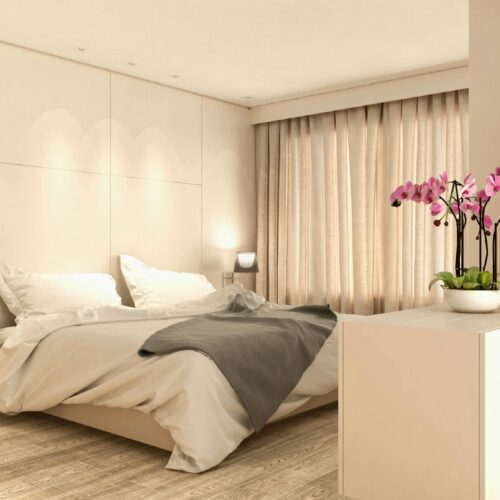 Interior de dormitorio moderno y elegante en Barcelona, con una cama grande, sábanas blancas, mesas de noche minimalistas y una planta orquídea. La luz natural entra a través de cortinas translúcidas, resaltando los materiales de alta calidad como el suelo de madera clara.