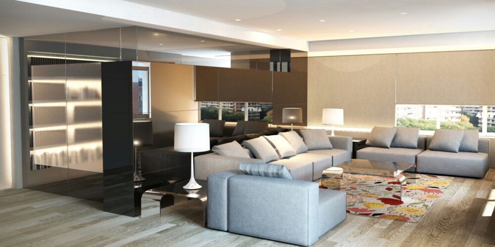 Moderna sala de estar en Barcelona con sofá gris y almohadas blancas, iluminada por luz natural a través de paredes de vidrio. Destacan los elementos de madera, una pared de acento negra y una alfombra floral.