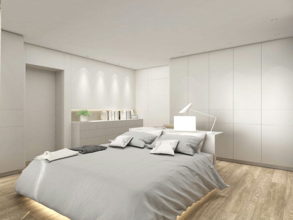 Diseño de interiores moderno en una habitación de lujo en Barcelona Diseño de interiores de una habitación contemporánea en Barcelona con una estética minimalista, que incluye una cama grande con ropa de cama gris suave, pisos de madera y armarios empotrados elegantes, resaltando la funcionalidad y la iluminación natural.