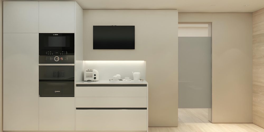 Cocina moderna con mobiliario blanco en un piso en Calle Cornet i Mas, que consta de electrodomésticos integrados que incluyen un microondas y un horno a la altura de los ojos, y suelo de madera clara. La encimera muestra una tostadora y vajilla, con un televisor de pantalla plana montado arriba, exhibiendo un diseño limpio y contemporáneo.