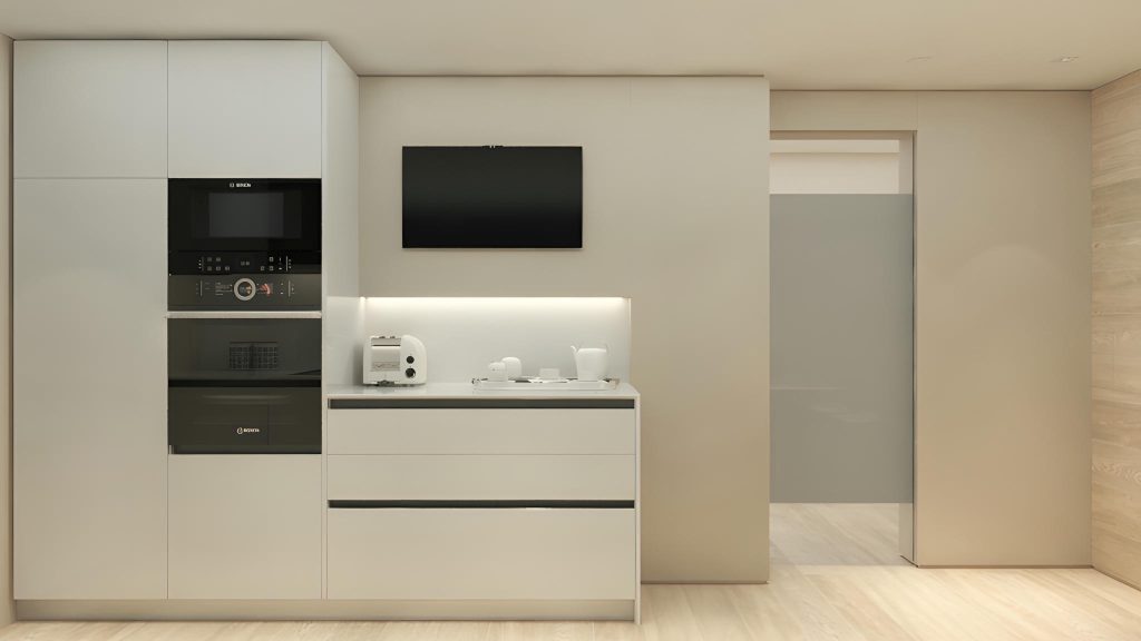 Cocina moderna con mobiliario blanco en un piso en Calle Cornet i Mas, que consta de electrodomésticos integrados que incluyen un microondas y un horno a la altura de los ojos, y suelo de madera clara. La encimera muestra una tostadora y vajilla, con un televisor de pantalla plana montado arriba, exhibiendo un diseño limpio y contemporáneo.