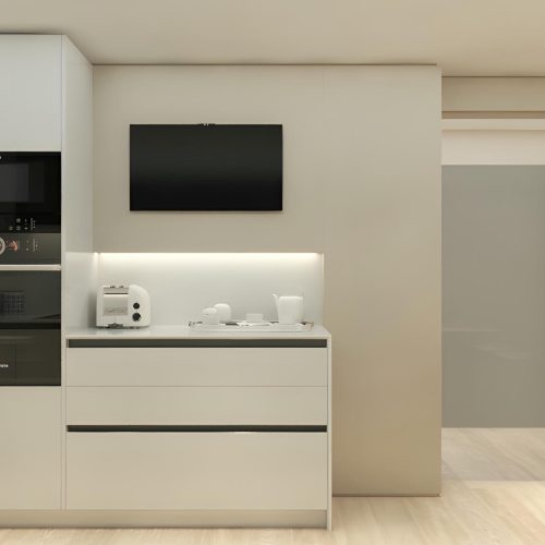 Cocina moderna con mobiliario blanco en un piso en Calle Cornet i Mas, que consta de electrodomésticos integrados que incluyen un microondas y un horno a la altura de los ojos, y suelo de madera clara. La encimera muestra una tostadora y vajilla, con un televisor de pantalla plana montado arriba, exhibiendo un diseño limpio y contemporáneo.