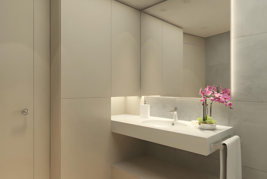 Un baño contemporáneo que presenta cabinetry estiloso de color beige claro, un amplio tocador blanco con un lavabo integrado y una maceta decorativa de orquídeas rosas. La suave iluminación indirecta realza la estética minimalista y la atmósfera, mientras que el suelo de madera de tono claro añade calidez y sofisticación. Una toalla colgada ordenadamente complementa el diseño moderno, creando un ambiente acogedor y limpio, adecuado para un hogar contemporáneo.