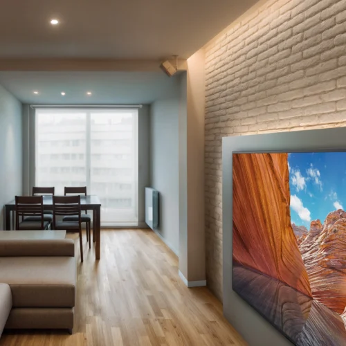 Piso en Calle Bolivia: Una sala de estar moderna con un sofá en forma de L de color claro, un gran televisor de pantalla plana que muestra un paisaje vívido de formaciones rocosas rojas contra un cielo azul, y una mesa de comedor rectangular con sillas de madera oscura cerca de una gran ventana que invita a la luz natural. Las paredes están pintadas en tonos neutros con una pared de ladrillo texturizado, y el suelo de madera clara realza la estética contemporánea.