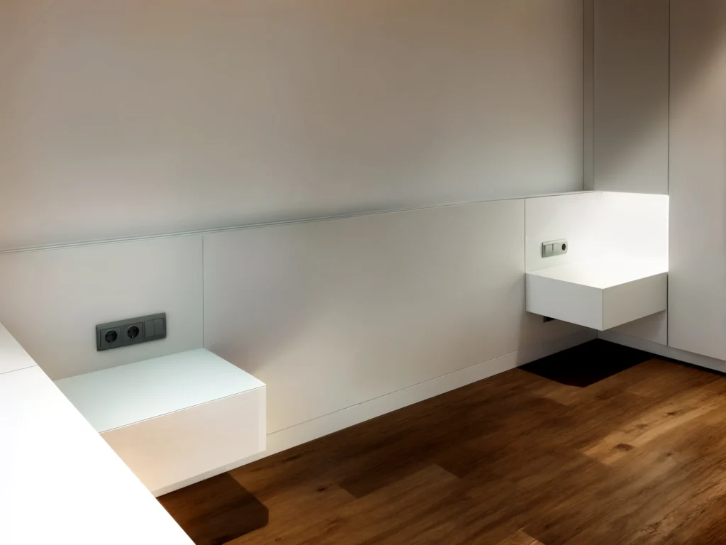 Diseño de interiores moderno en Barcelona: Espacio minimalista de alta gama Espacio interior minimalista en Barcelona con mobiliario de diseño moderno, armarios blancos, estanterías flotantes y suelo de madera, resaltando funcionalidad y estética.