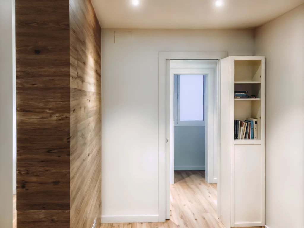 Diseño de Interiores Moderno en Barcelona con Elementos de Madera y Luz Natural Espacio interior contemporáneo en Barcelona con diseño de alta gama, destacando una pared de madera, estantería blanca y un pasillo iluminado por luz natural.