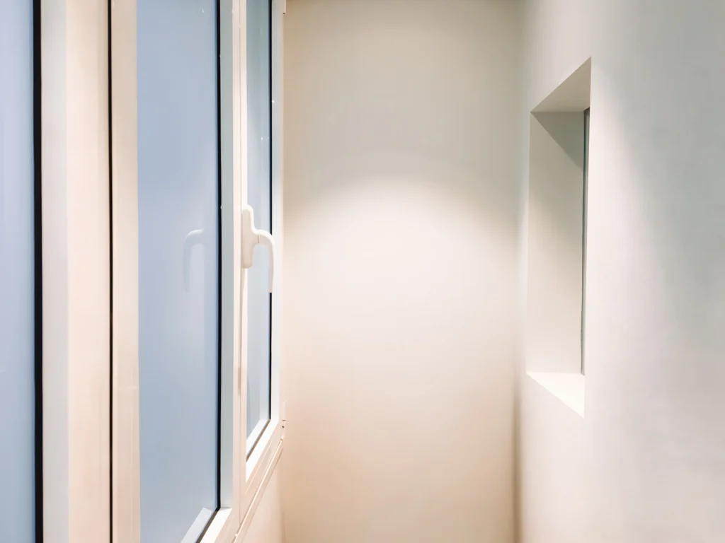 Diseño de interiores moderno en Barcelona con luz natural Esquina de un espacio moderno en Barcelona que muestra una pared de color claro y grandes ventanales, enfatizando el diseño minimalista, líneas limpias y detalles arquitectónicos contemporáneos.