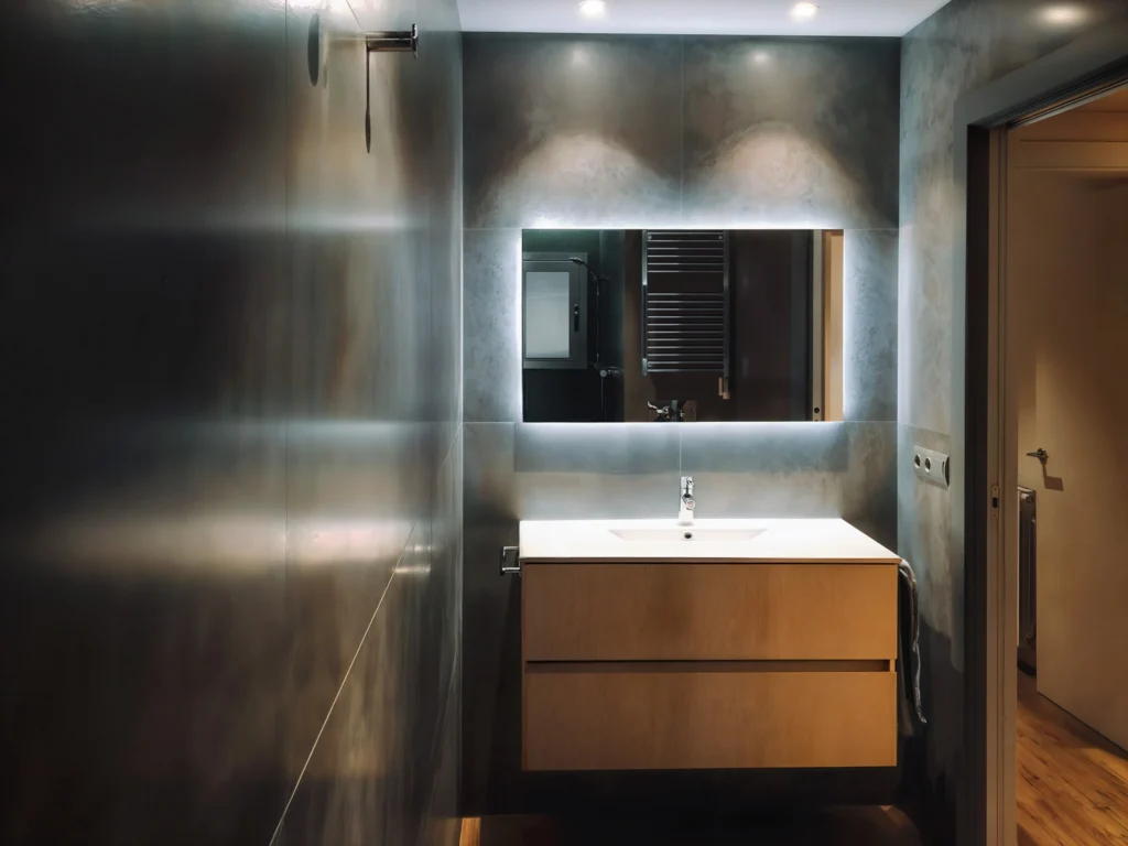 Baño Moderno de Diseño Interior en Barcelona Interior de baño contemporáneo en Barcelona con mobiliario de alta gama, incluyendo un tocador de madera clara y lavabo blanco en un ambiente elegante.