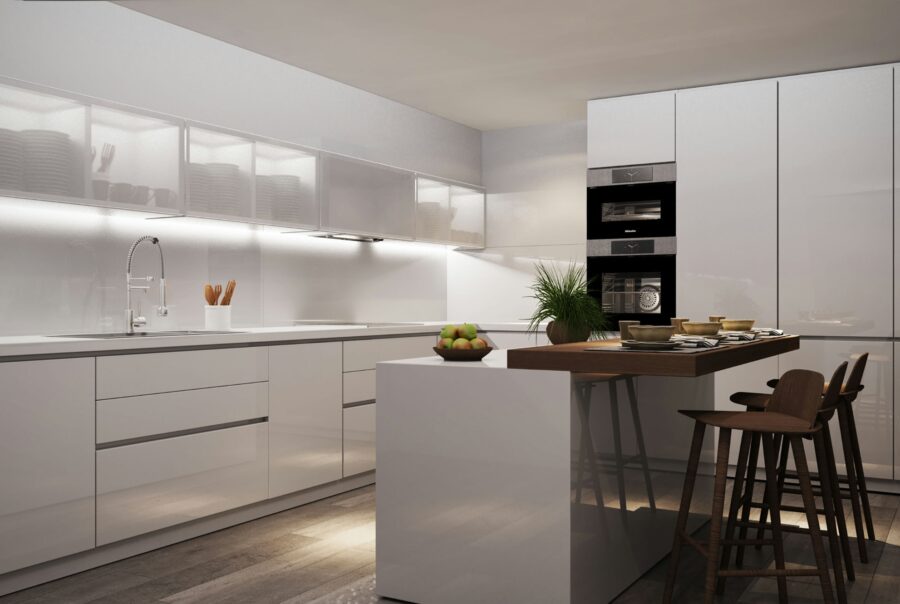 Cocina de lujo en Barcelona con diseño moderno, muebles blancos brillantes, isla central con taburetes de madera y superficies de mármol. Espacio iluminado naturalmente, destacando la estética contemporánea y detalles arquitectónicos elegantes.