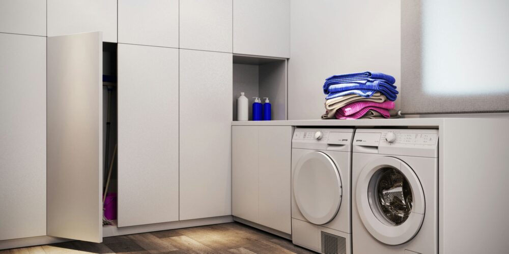 Lavandería contemporánea en Barcelona con mobiliario blanco, dos lavadoras modernas y toallas coloridas sobre una encimera. Suelo de madera y luz natural realzan la estética elegante y funcional del espacio.