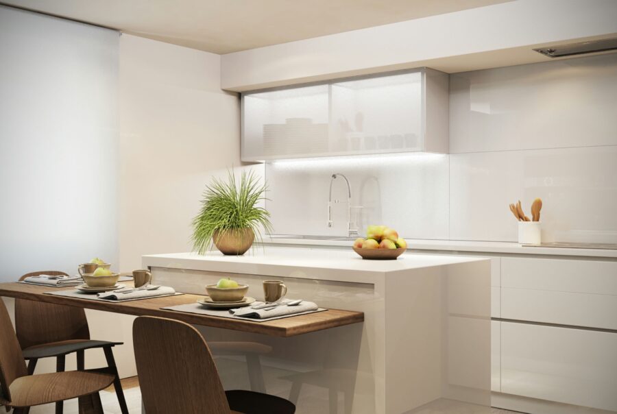 Moderna cocina de diseño interior en Barcelona, destacando una isla central blanca, mesa de madera, utensilios de cocina y frutera con manzanas, iluminada de manera natural.