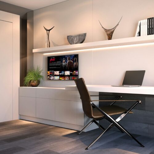 Oficina moderna en Barcelona con escritorio blanco, silla negra, estante flotante y pantalla de televisión, iluminada con luz natural