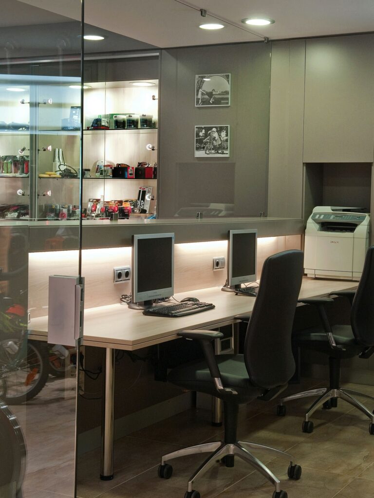 Diseño de interiores moderno en Barcelona: espacio de trabajo elegante Espacio de trabajo contemporáneo en Barcelona con escritorios de ordenador y sillas ergonómicas, elementos de piedra y cristal, y una vitrina iluminada mostrando decoraciones de calidad.