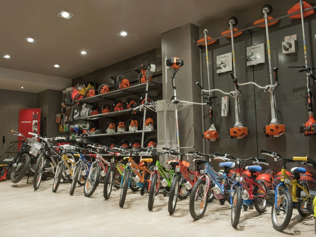 Espacio Retail Vibrante que Muestra Bicicletas y Equipos de Exterior Una tienda de retail bien organizada con una variedad de bicicletas en diferentes colores y tamaños a la izquierda, con estantes llenos de herramientas de exterior y equipos de jardinería en el fondo, iluminada por luces brillantes en el techo.