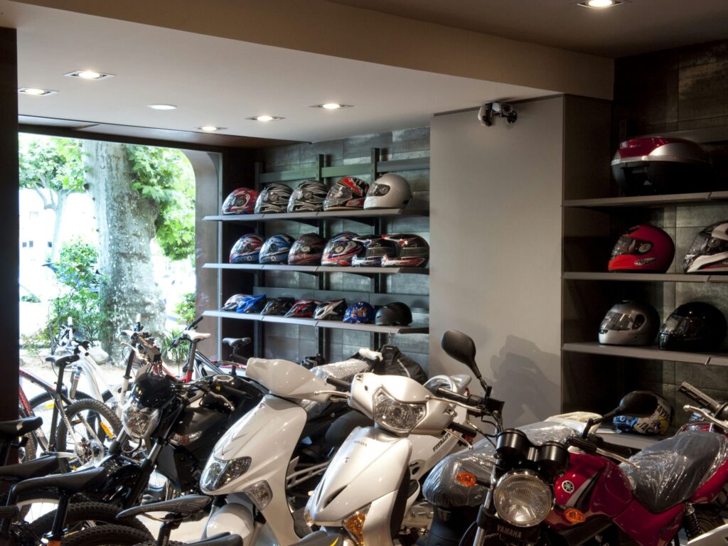 Tienda Moderna de Motocicletas y Bicicletas con Cascos y Vehículos Elegantes Una vibrante tienda de motocicletas y bicicletas que presenta una variedad de motocicletas y bicicletas en primer plano, con cascos coloridos exhibidos en estantes elegantes en un interior moderno y bien iluminado, potenciado por la luz natural que entra a través de grandes ventanas.