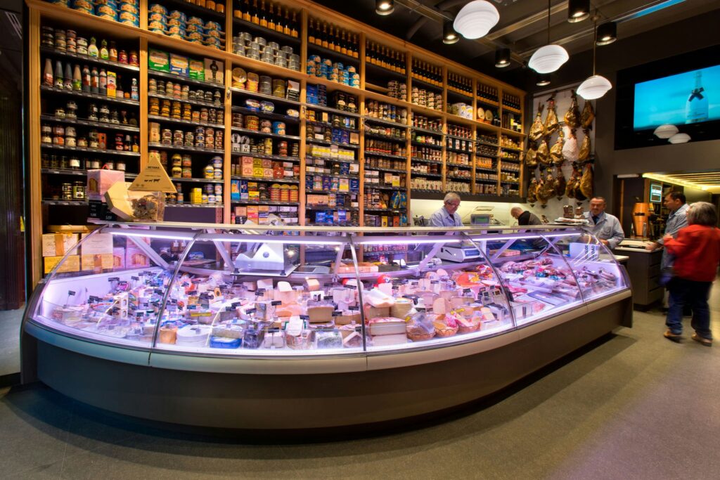 Diseño de interiores de una tienda gourmet en Barcelona Interior vibrante de una tienda gourmet en Barcelona, con un mostrador curvado de vidrio lleno de quesos artesanales y productos gourmet, iluminado con luces suaves.