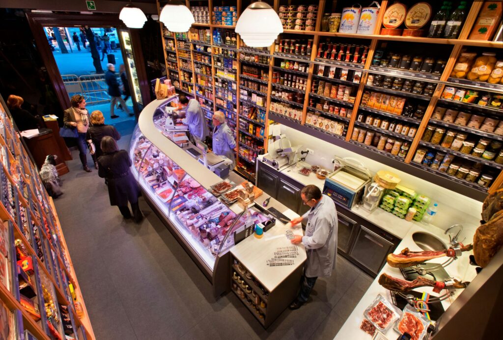 Interior Gourmet de un Tienda en Barcelona: Diseño Moderno y Funcionalidad Vibrante interior de una tienda gourmet en Barcelona con un mostrador curvo exhibiendo carnes frescas y productos gourmet, rodeado de estantes de alta calidad y clientes interactuando.