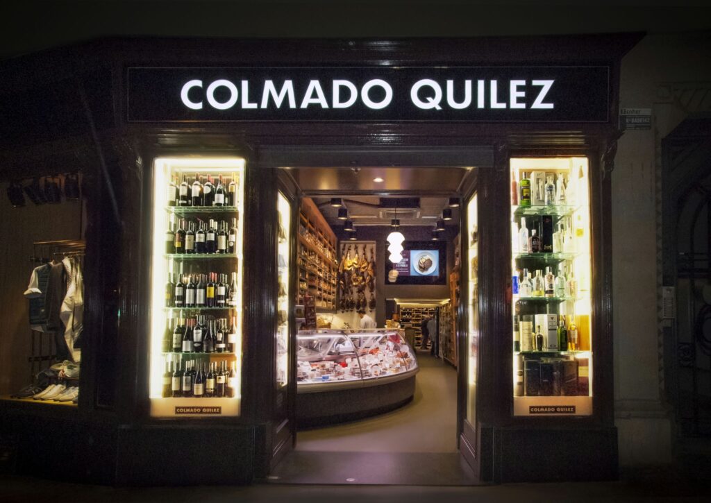Colmado Quilez: Tienda Gourmet de Alta Gama en Barcelona Exteriores de Colmado Quilez en Barcelona, destacando la elegante entrada y la vitrina iluminada con vinos y productos gourmet.