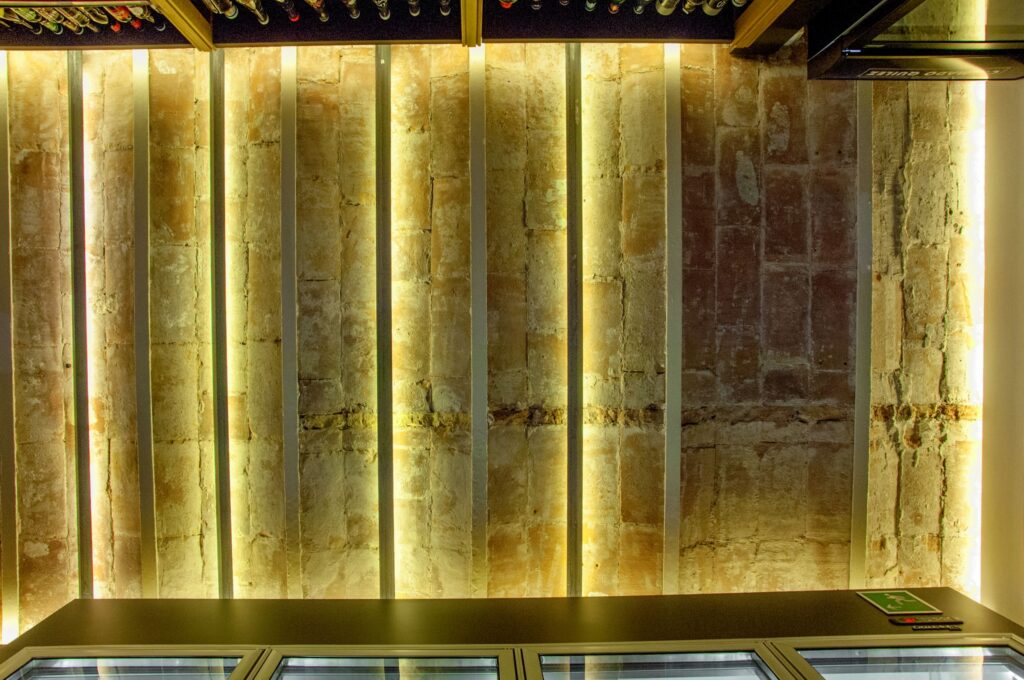 Diseño de Interiores Modernos en Barcelona: Arquitectura de Alta Gama Proyecto de diseño de interiores en Barcelona que muestra una arquitectura moderna con vigas de madera iluminadas y ladrillos expuestos, resaltando la combinación de estética contemporánea y materiales de alta calidad.