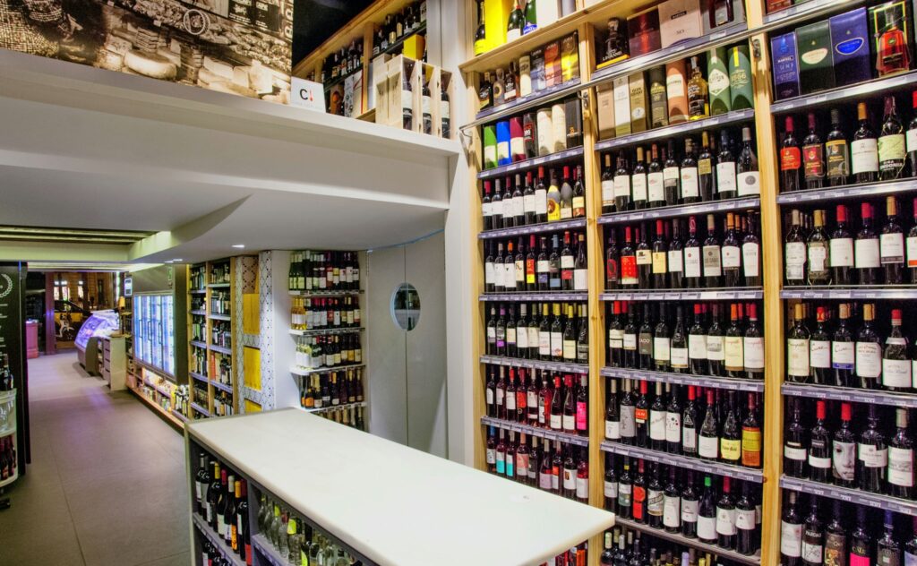 Diseño de Interiores de Tienda de Vinos de Alta Gama en Barcelona Interior moderno de una tienda de vinos de alta gama en Barcelona, con estanterías llenas de botellas de vino de calidad y una barra funcional, iluminada por luz natural.