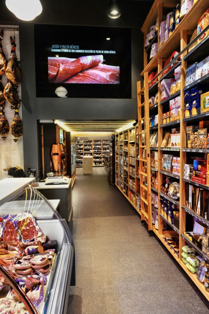 Diseño de Interiores en Tienda Gourmet de Alta Gama en Barcelona Vista interior de una tienda gourmet de lujo en Barcelona, con diseño moderno y contemporáneo, exhibiendo estanterías organizadas de alimentos gourmet y detalles arquitectónicos sofisticados.