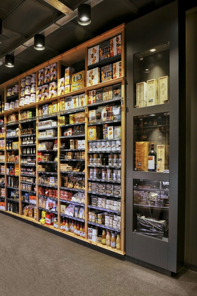 Diseño de interiores moderno en Barcelona con estantería de productos gourmet Estantería moderna en diseño de interiores de alta gama en Barcelona, exhibiendo productos gourmet y enfatizando la funcionalidad y estética con materiales de madera y negro.